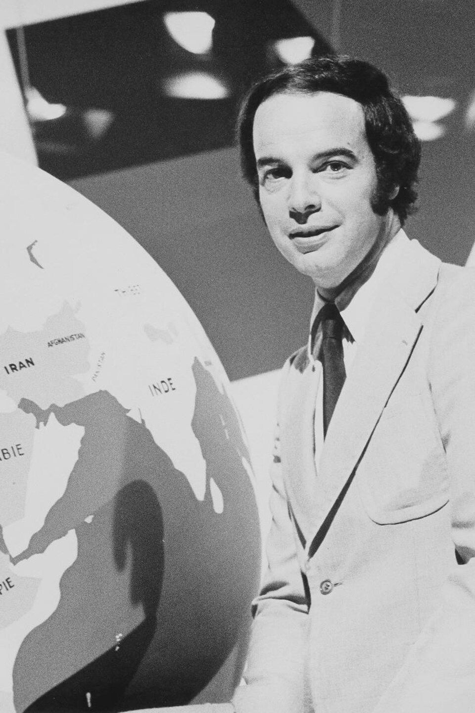 Pierre Nadeau pose à côté d'un globe terrestre.