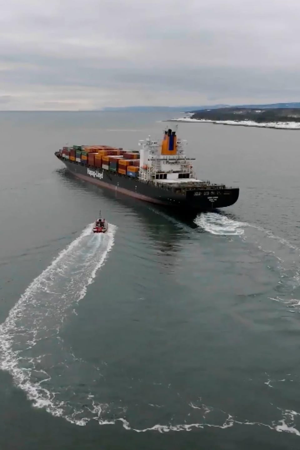 Vue aérienne d'un petit bateau-pilote s'approchant d'un immense porte-conteneurs.