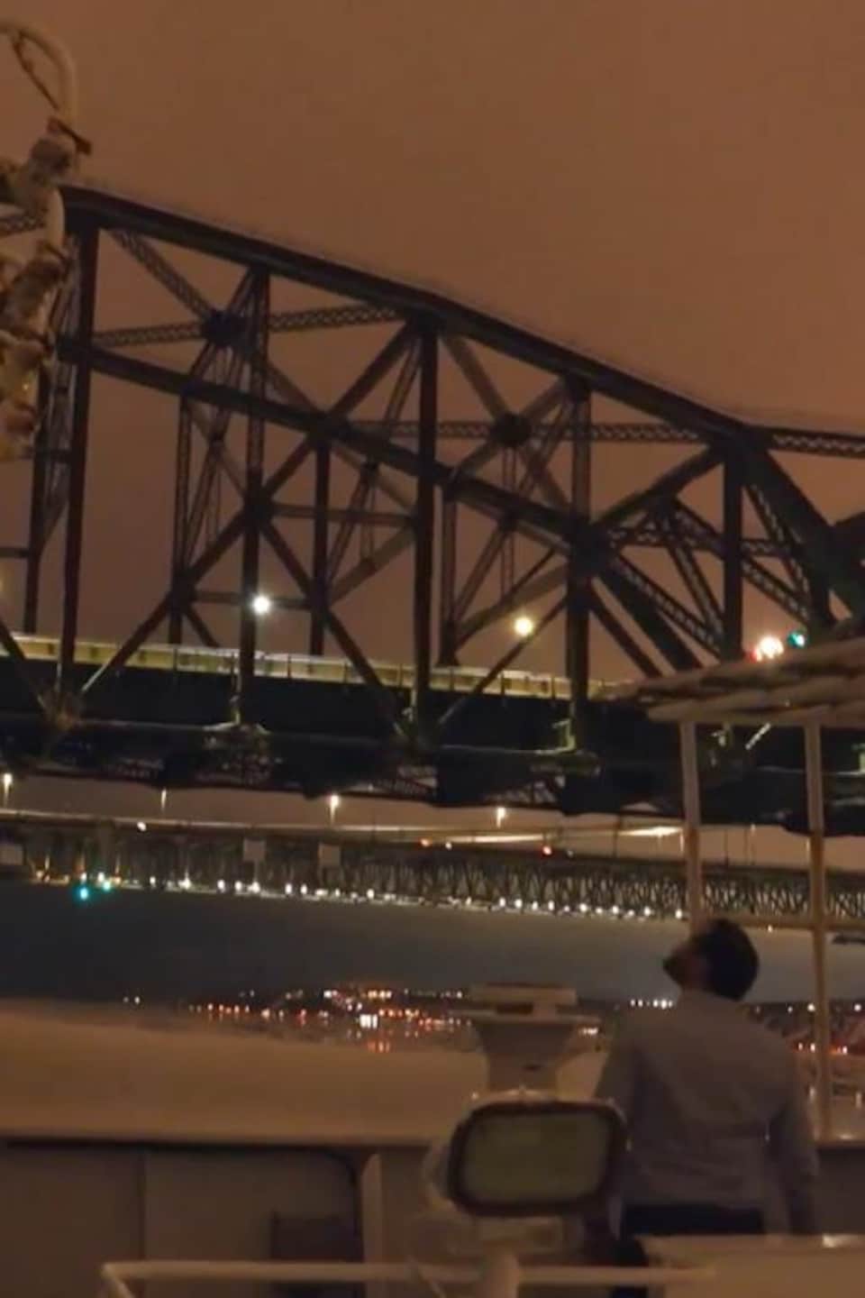 Un pilote et un capitaine surveillent le passage d'un navire sous les ponts de Québec en pleine nuit.