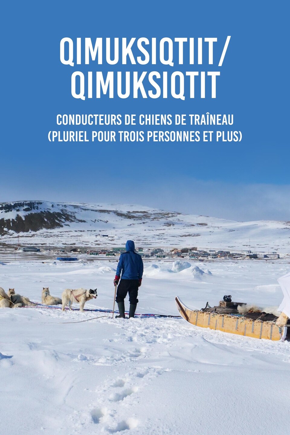 Le mot en inuktitut « qimuksiqtiit » ou « qimuksiqtit » et sa traduction en français, conducteurs de chiens de traîneau au pluriel écrit sur une photo de Devon Manik de dos avec ses chiens et son traîneau devant Resolute Bay, au mois de juin, dans le nord du Nunavut.