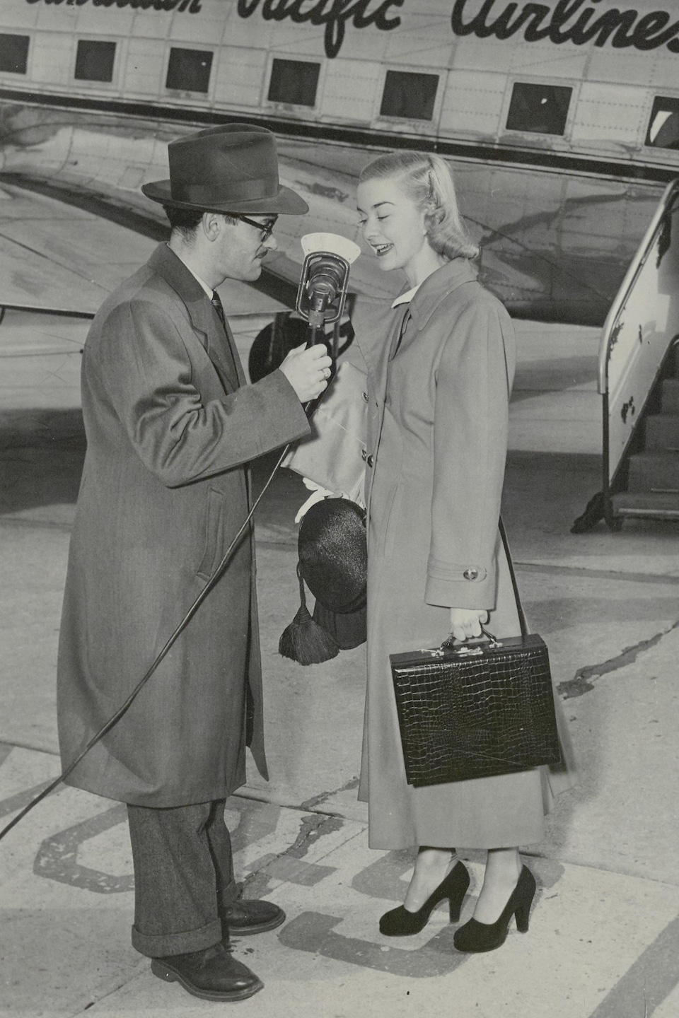 Barbara Ann Scott et Lionel Morin avec son micro sur le tarmac avec un avion en arrière-plan.