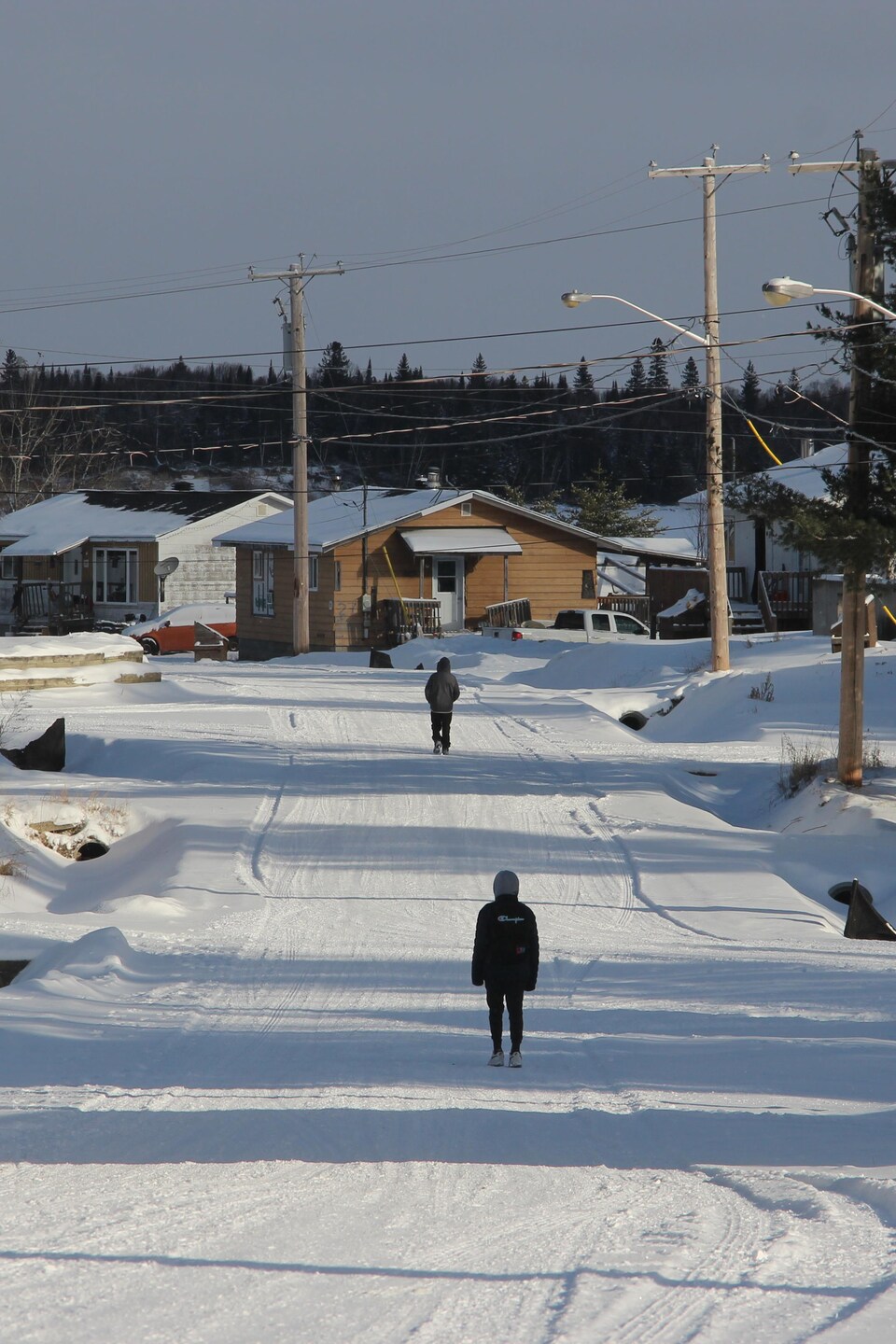 Vue d'ensemble de la communauté : des maisons, un chemin enneigé et deux personnes qui marchent sur le chemin. 