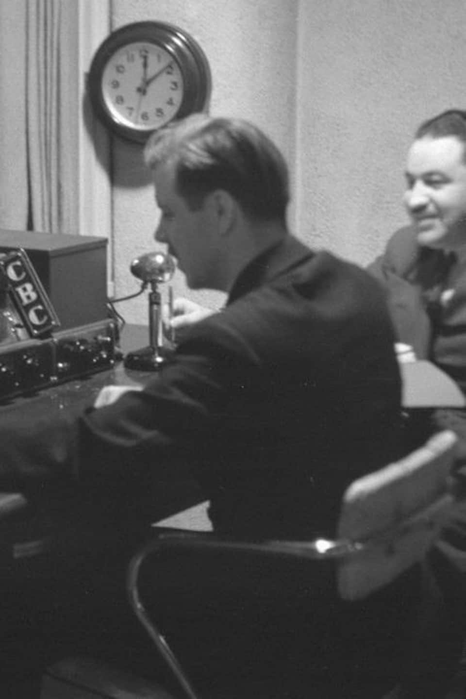 En régie, dans un studio de radio, le technicien opérateur et le réalisateur, assis devant la boîte de sonorisation et un micro.