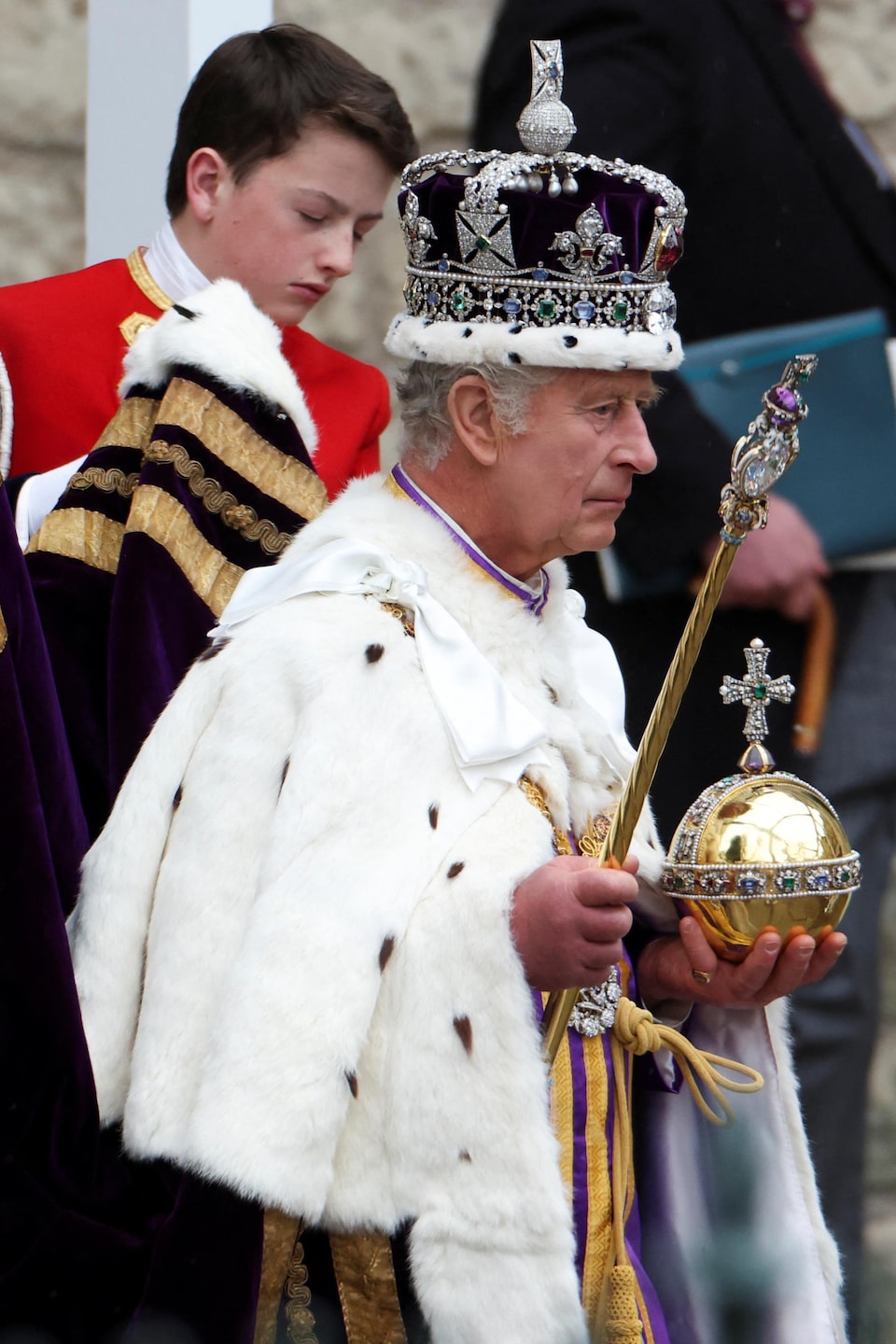 Le roi Charles III regarde vers l'avant alors que des enfants tiennent sa toge.