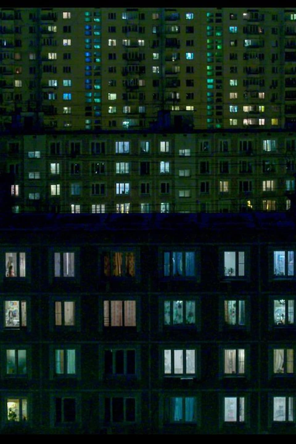 Les fenêtres de nombreux immeubles d'habitation sont éclairées dans la noirceur du soir.