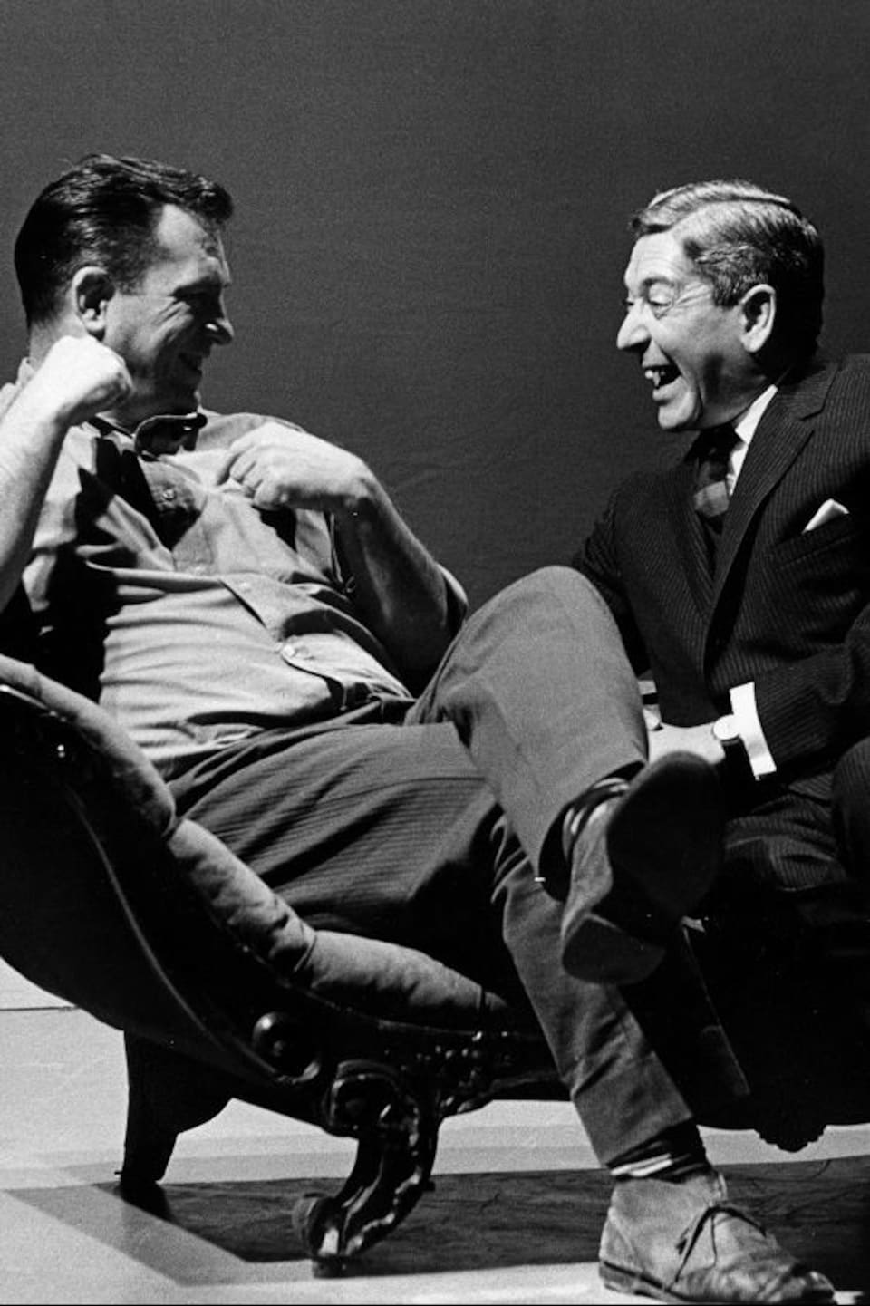 Dans un studio de télévision, l'écrivain américain Jack Kerouac et l'animateur Fernand Seguin, riant, sont assis sur une causeuse.