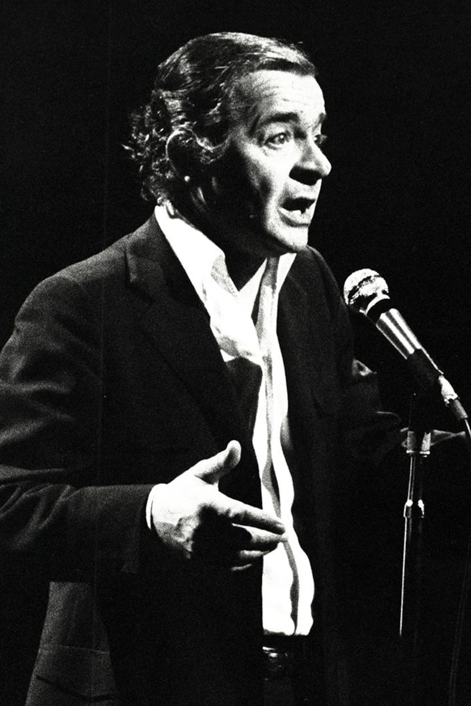 Serge Reggiani qui chante debout sur scène derrière un micro sur pied.