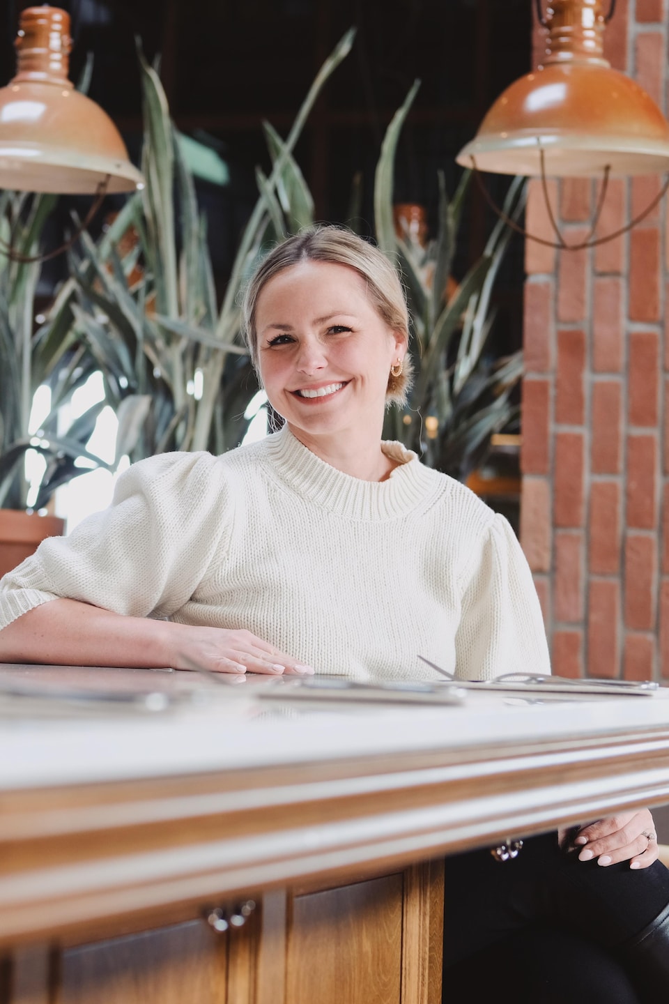 Sophie Marchand, jeune femme aux cheveux blonds, est assise au comptoir de Chez Boulay. Le décor est accentué de verdure et de teintes de cuivre. 