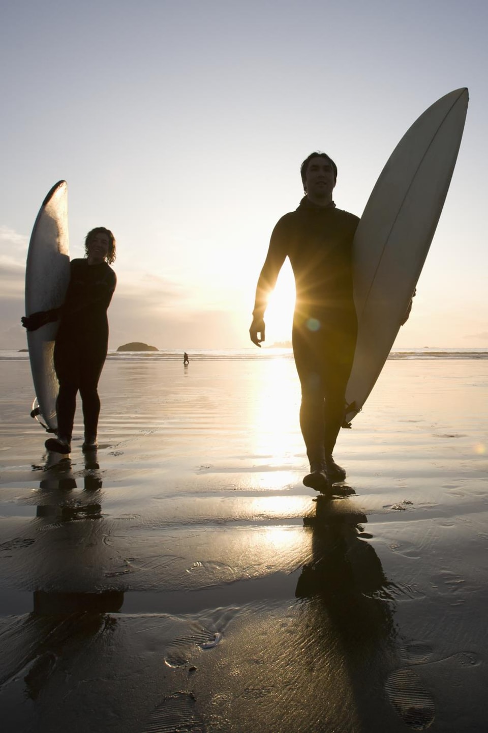 Silhouettes de trois surfeurs sortant de l'eau sur la plage Chesterman, à Tofino.
