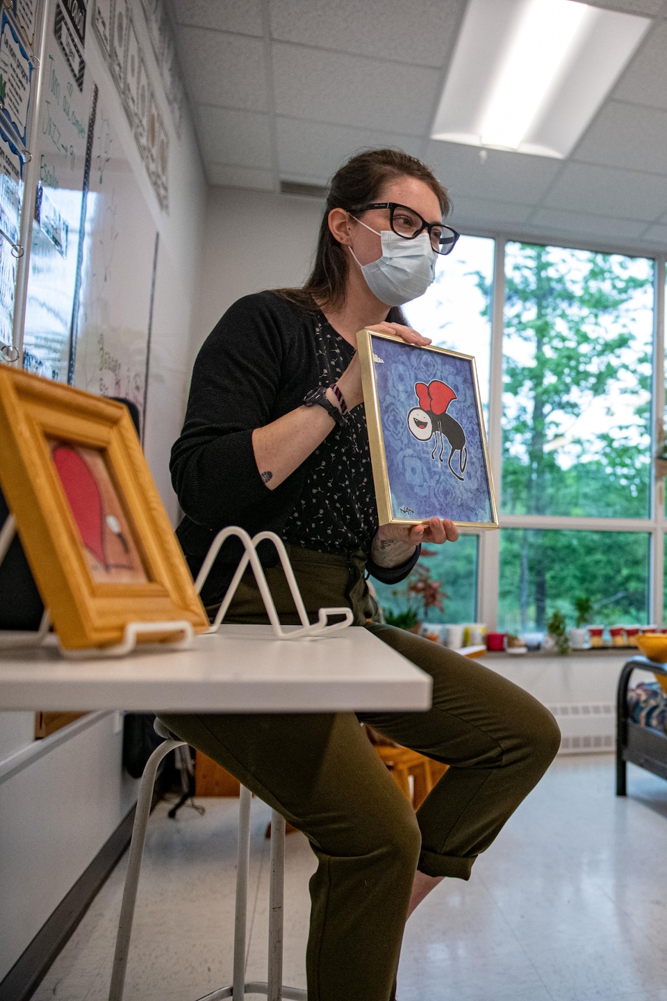 Une enseignante assise sur un tabouret devant une classe. Elle tient dans ses mains un cadre avec une oeuvre d'Ultra Nan. 