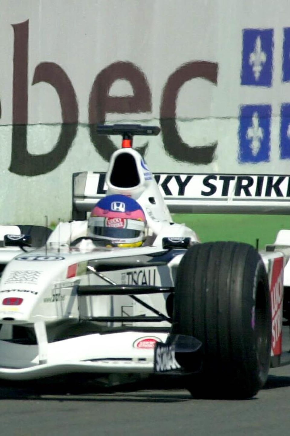 Une publicité gouvernementale peinte sur un mur dit : "Bonjour Québec" alors que la voiture de Jacques Villeneuve passe devant.