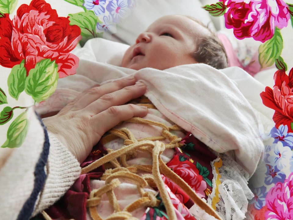 Un bébé avec la main de sa mère et un graphisme fleuri.