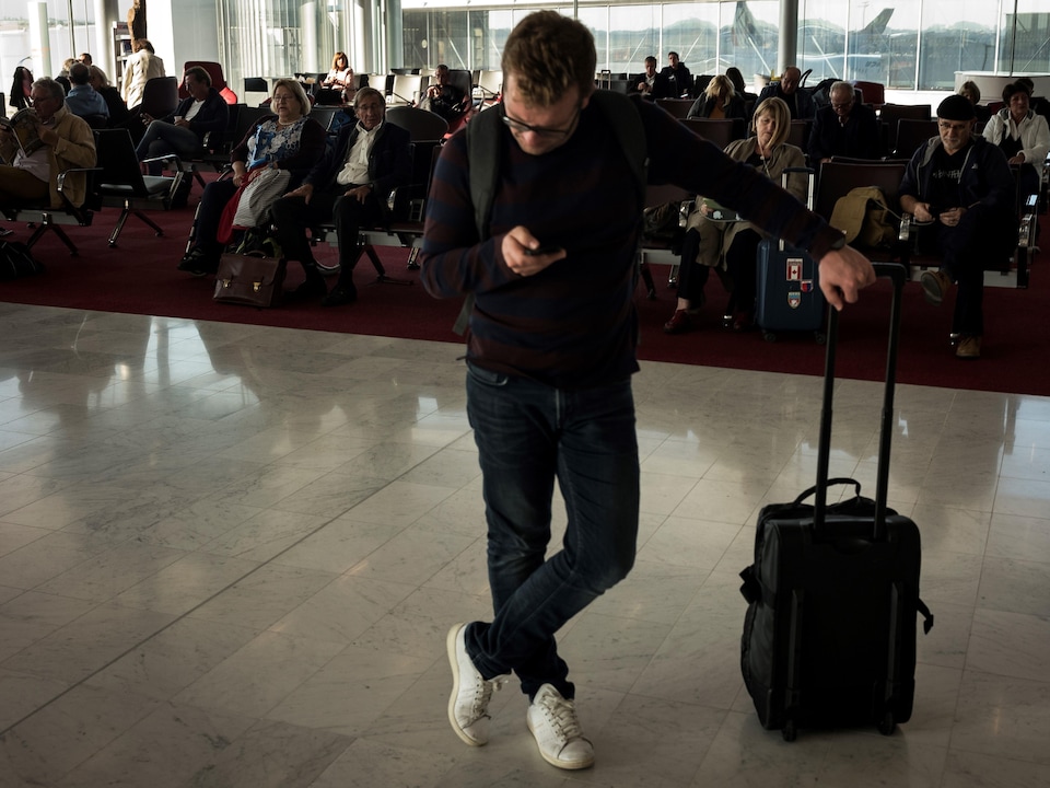 Un homme s'appuie sur sa valise tout en regardant son téléphone portable dans une salle d'attente.