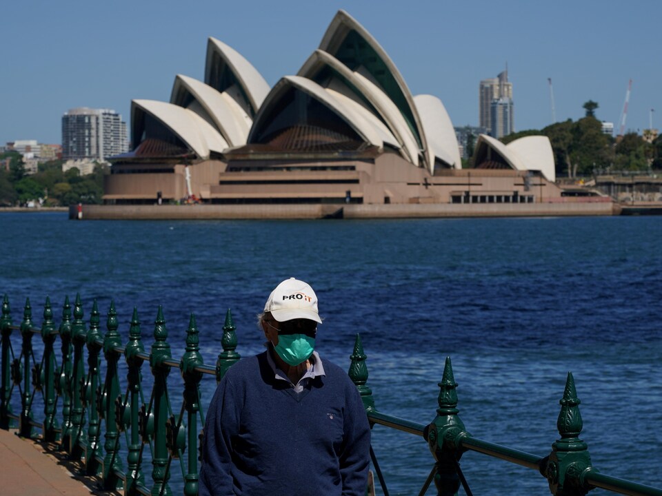 A masked man walks in front of the Sydney Opera House.