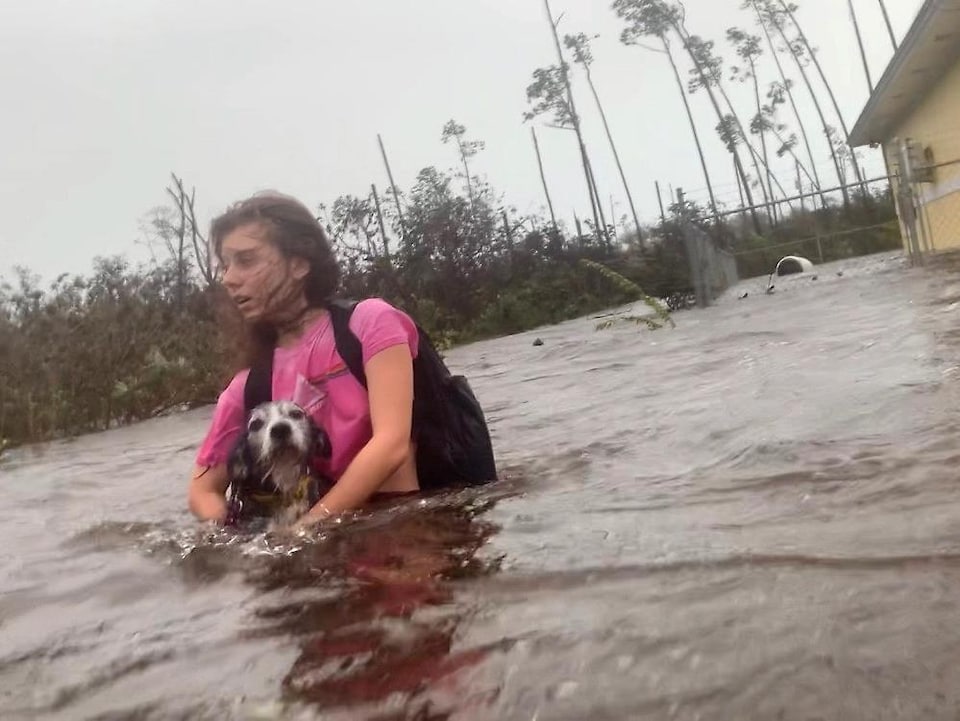 Une adolescente tient un chien dans ses bras en marchant dans une rue inondée.