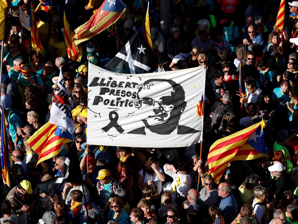 Un plan en plongée montre une foule qui tient des affiches et des drapeaux catalans.