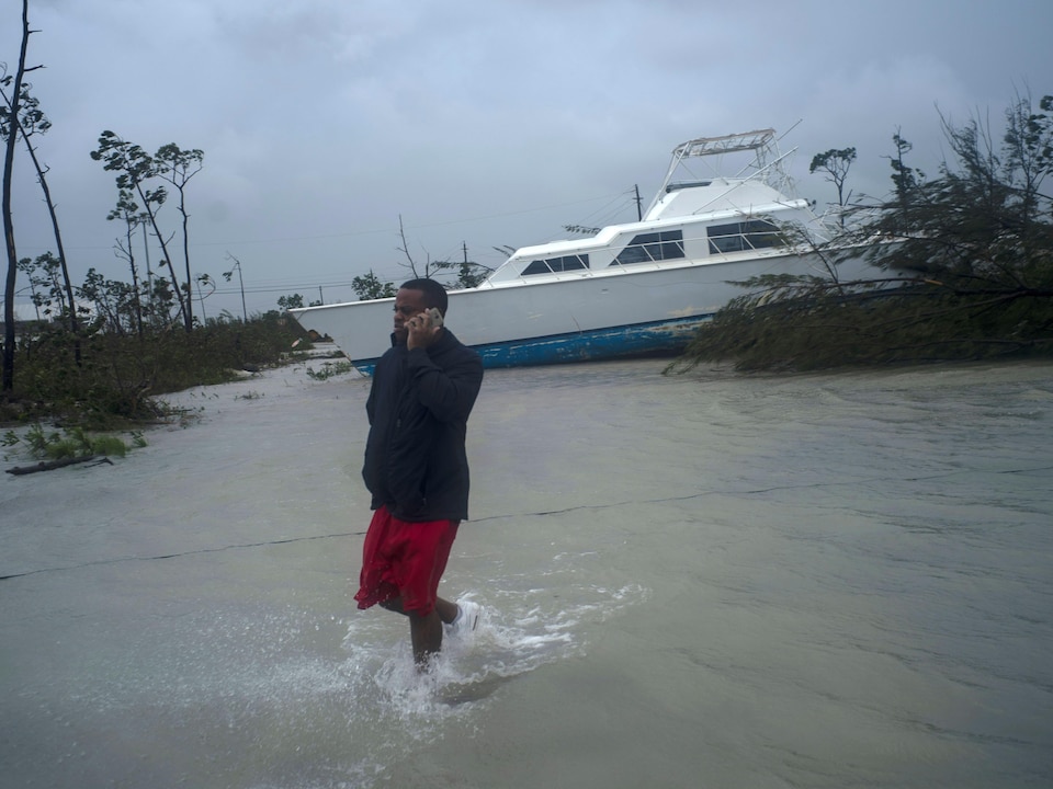 Un homme parle au téléphone cellulaire près d'un bateau échoué dans les terres.