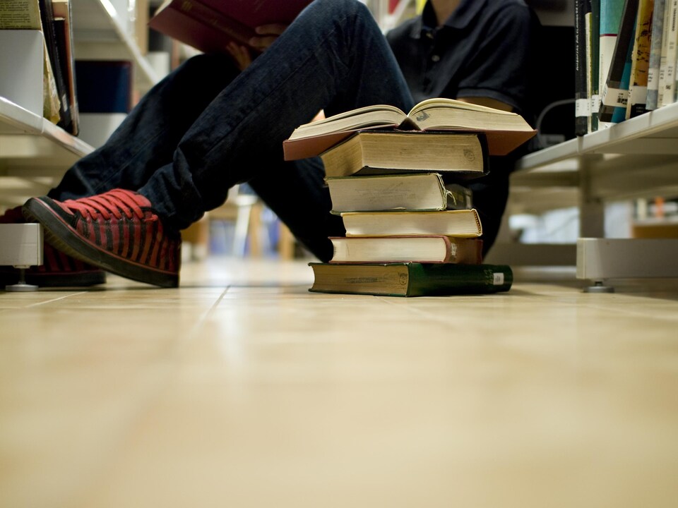 Un étudiant consulte des livres assis par terre dans la bibliothèque d'une école secondaire. 