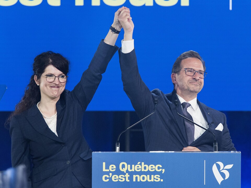 Yves-François Blanchet et sa conjointe les mains en l'air sur la scène devant les partisans du Bloc québécois.