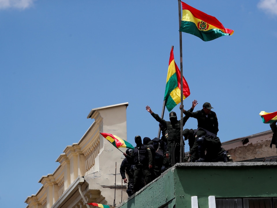 Des policiers en uniformes noirs se tiennent sur le toit d'un commissariat en brandissant le drapeau de la Bolivie. 