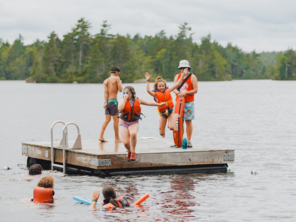 Des enfants se baignent dans un lac, surveillés par un moniteur du camp d'été.