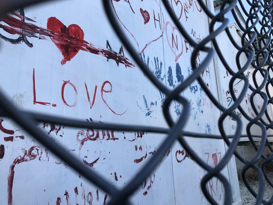 Derrière une clôture métallique, un mur de conteneur sur lequel est écrit «love» avec un coeur rouge.