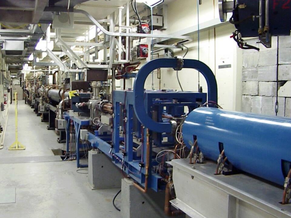 On voit un gros cylindre métallique bleu et d'autres tuyaux et câbles alignés dans les installations du synchrotron.