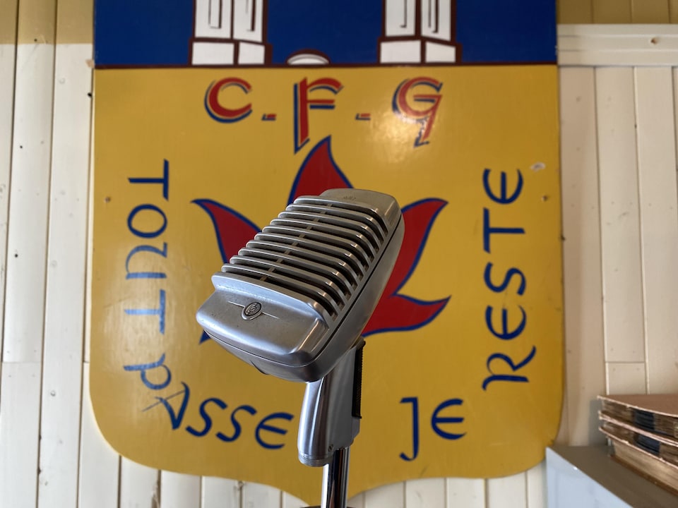 Un microphone de CFRG devant un emblème de la station où il est inscrit «Tout passe, je reste».