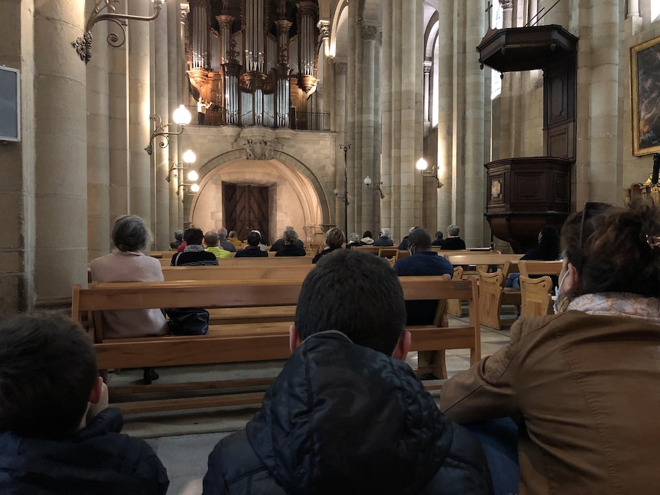 On voit de dos les gens assis dans la cathédrale qui assistent au concert. Au fond en haut, l'orgue de la cathédrale.