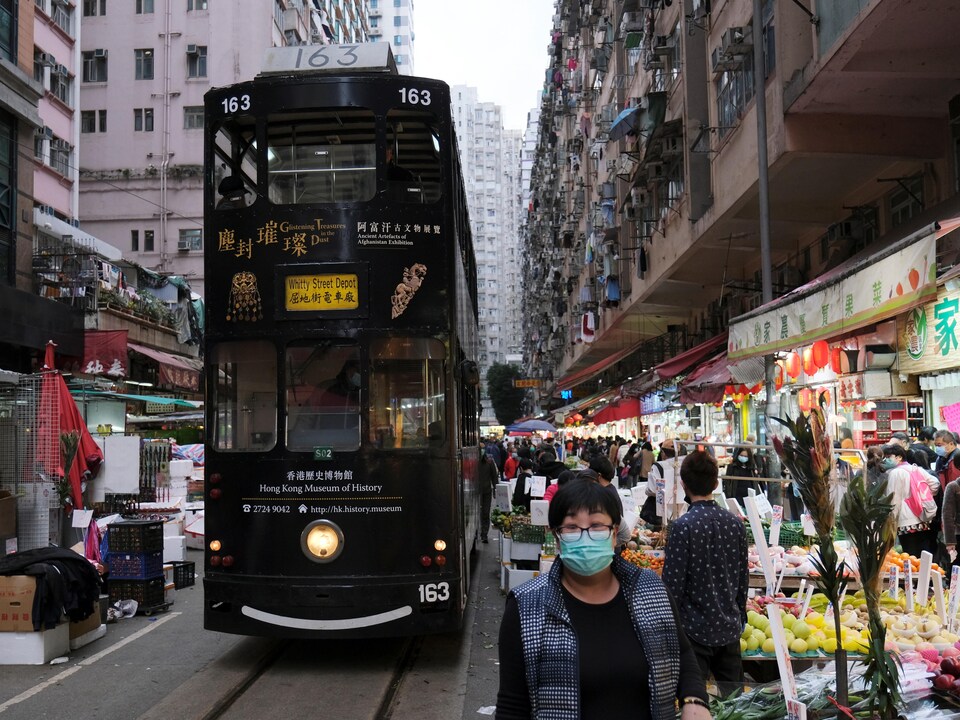 Des personnes portant des masques respiratoires circulent dans un marché, près duquel passe un tramway.