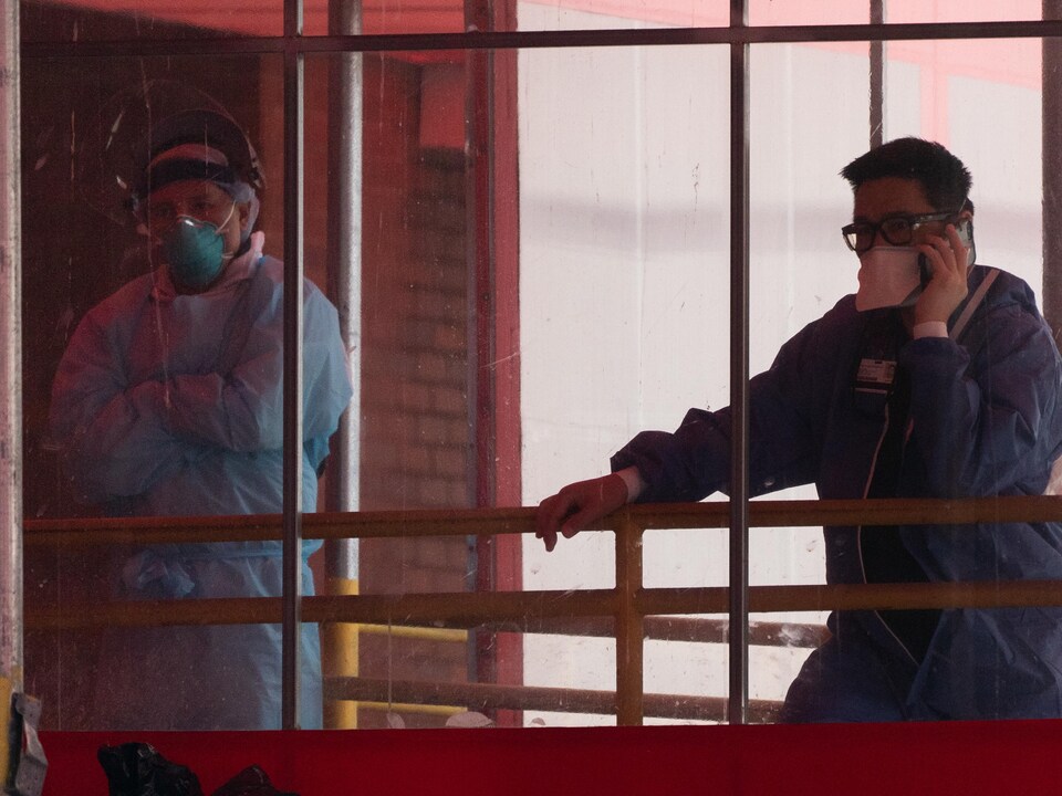 Two employees wearing medical coveralls take a break behind a window at a New York hospital.