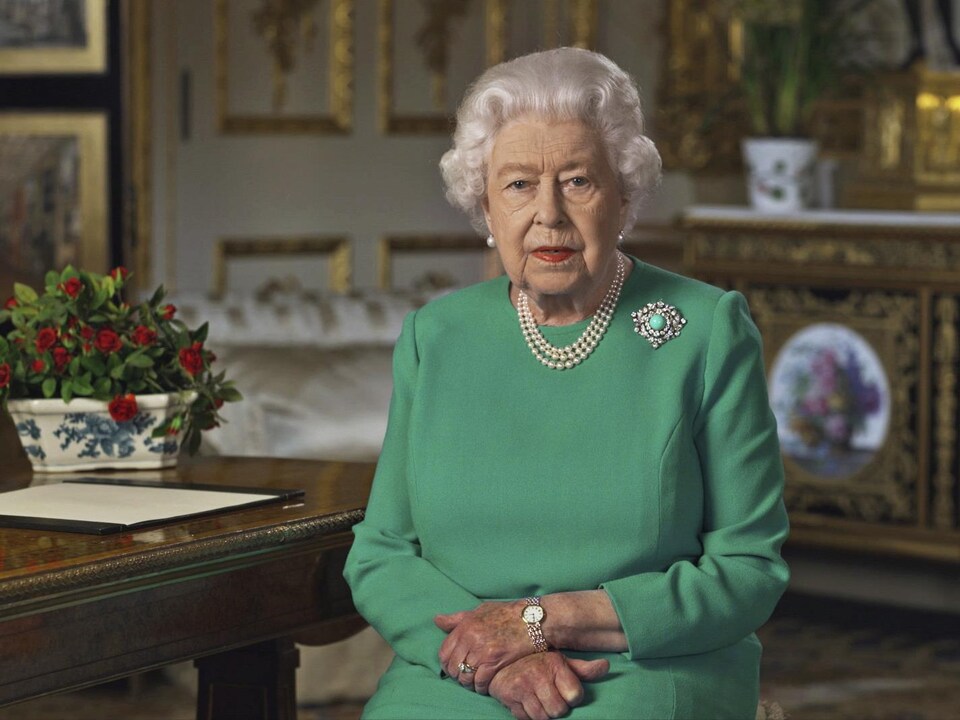 La reine Élisabeth II assise à un bureau dans une salle du château de Windsor. 