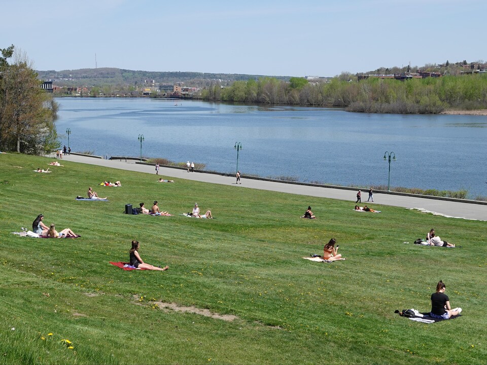 Plusieurs personnes assises sur le gazon respectent la distanciation physique près du lac des Nations à Sherbrooke.