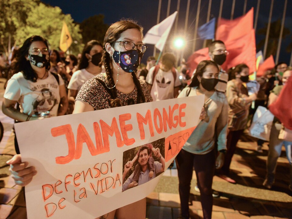 Une femme tient une banderole avec le nom de Jaime Monje, un environnementaliste assassiné. 