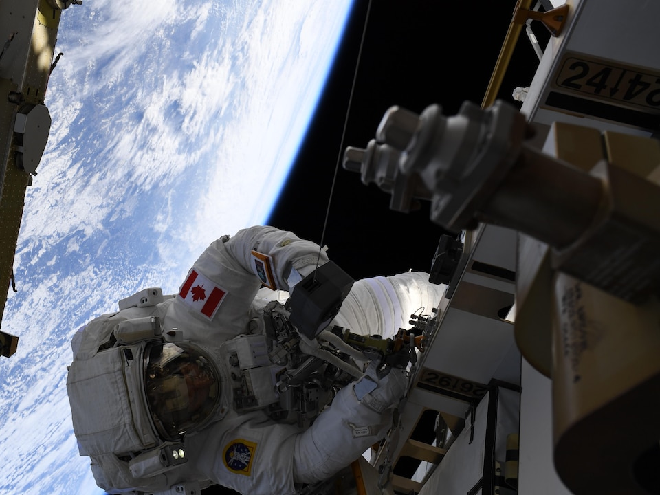 David Saint-Jacques procède à des travaux sur la Station spatiale internationale, avec la Terre en arrière-plan. 
