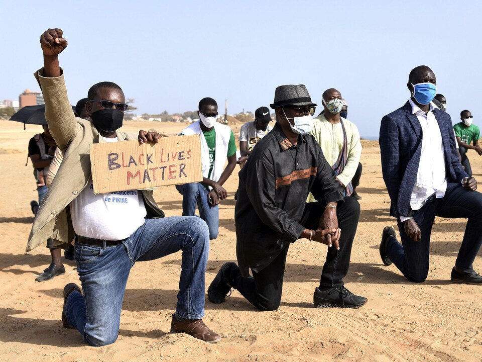 Des manifestants, dont un brandissant le poing et tenant un écriteau de Black Lives Matter, à genoux sur le sable de Dakar, au Sénégal.