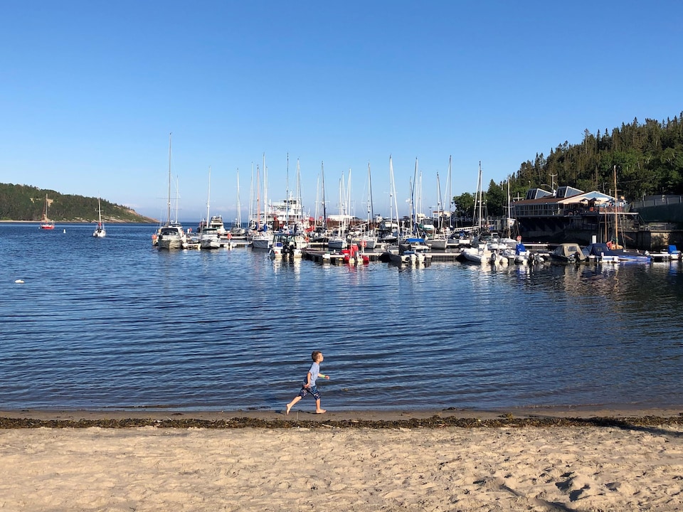 Des bateaux sur l'eau et un enfant qui court sur la plage.