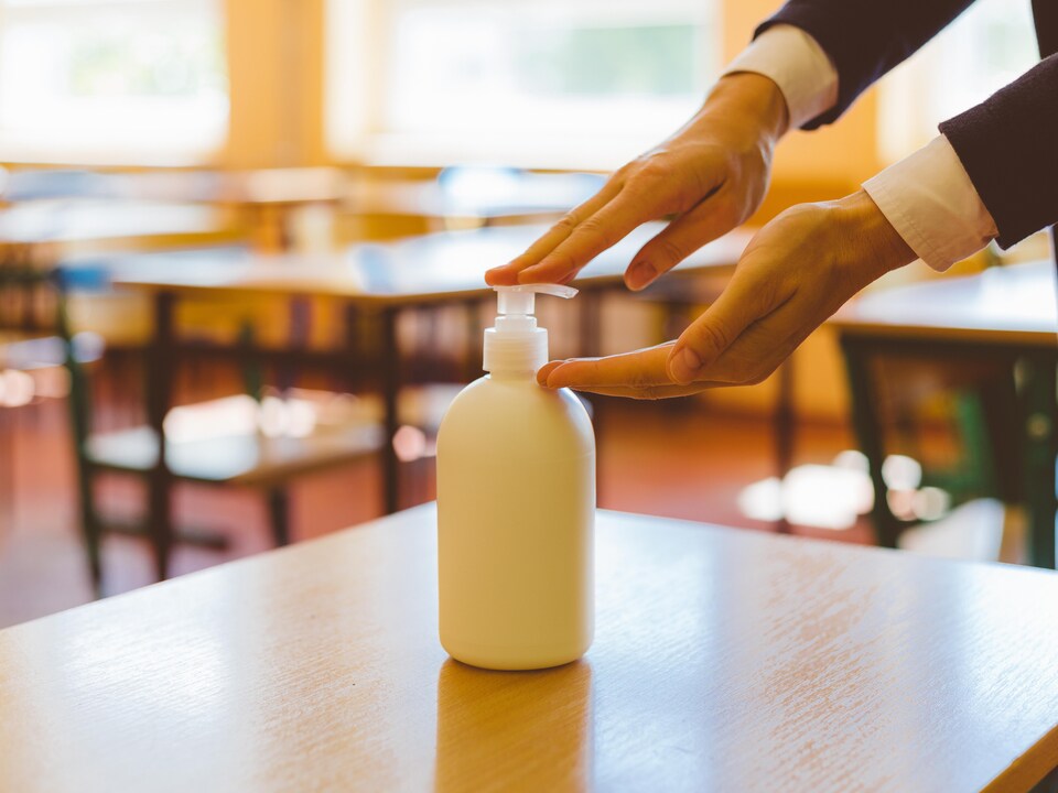 Les mains d'une enseignante qui appuie sur le bouchon d'une bouteille de désinfectant posée sur un pupitre dans une salle de classe.