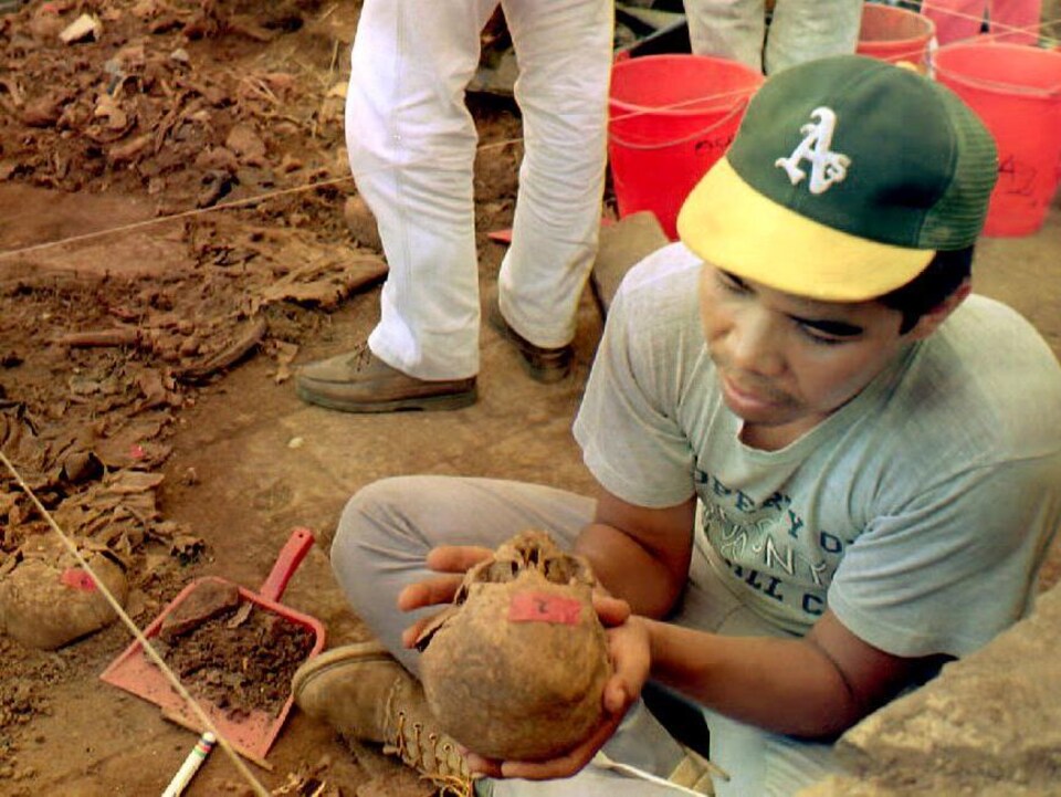 Un homme assis sur le sol tient un crâne dans sa main.