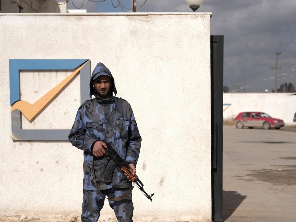 Un homme armé est debout devant un mur sur lequel on peut voir un crochet dans une case.