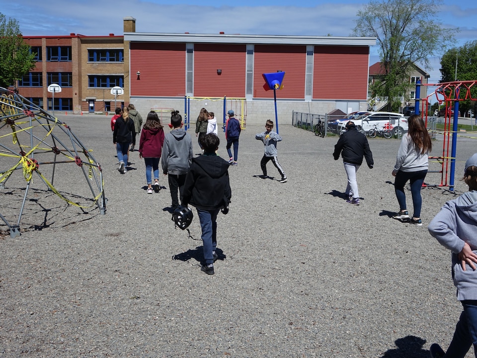14 élèves tentent de garder une distance de deux mètres entre eux en marchant à la queue leu leu vers l'école.