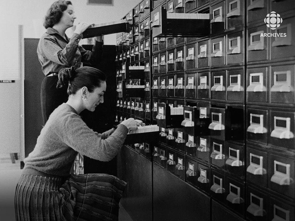 Deux employées, Jacqueline Farley et Charlotte Ferland, consultent des fiches dans un classeur.