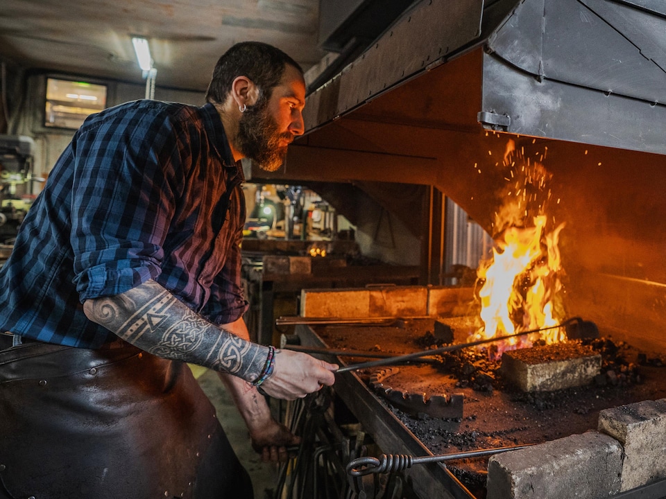 Romain Francès fait chauffer du métal près d'une flamme dans sa forge.