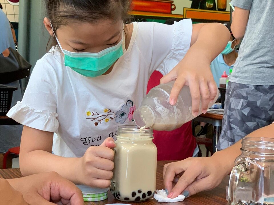 Une jeune fille se verse la boisson dans son pot, l'appétit se lit dans ses yeux.