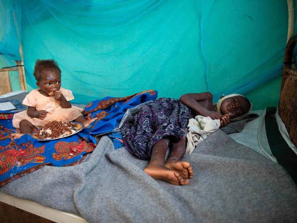Un jeune garçon malade sur un lit, avec un bébé juste à côté.