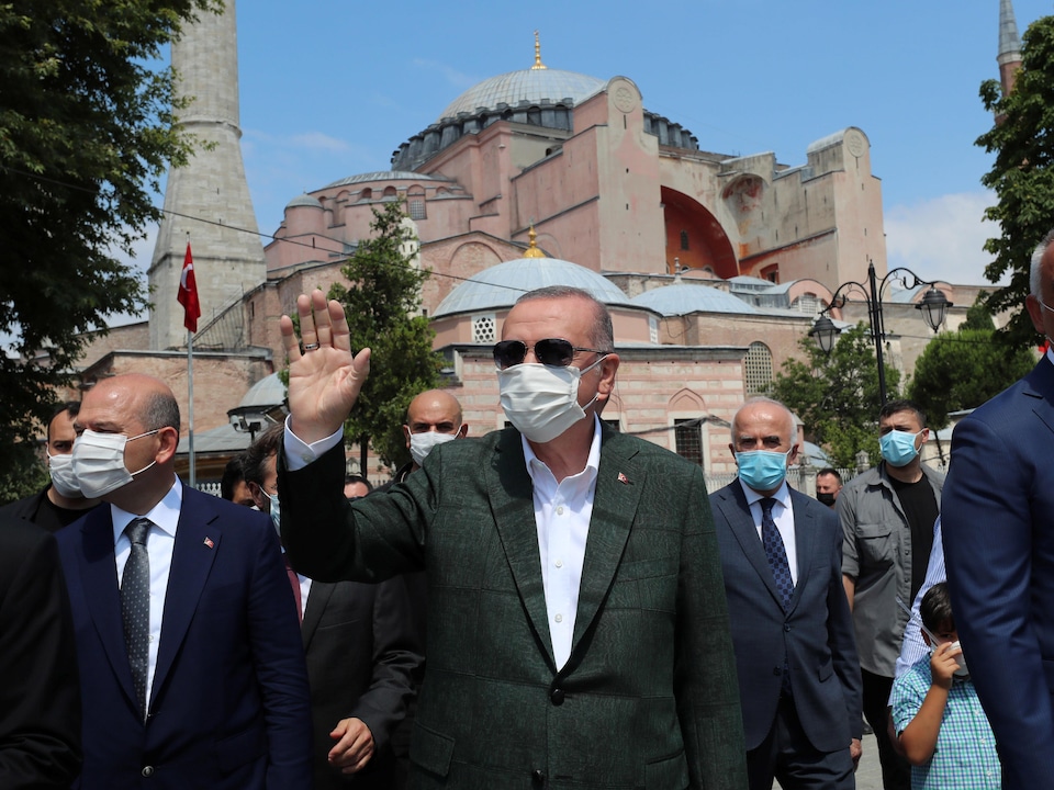 Masqué, le président turc salue la foule. On fond, on aperçoit l'imposant édifice.