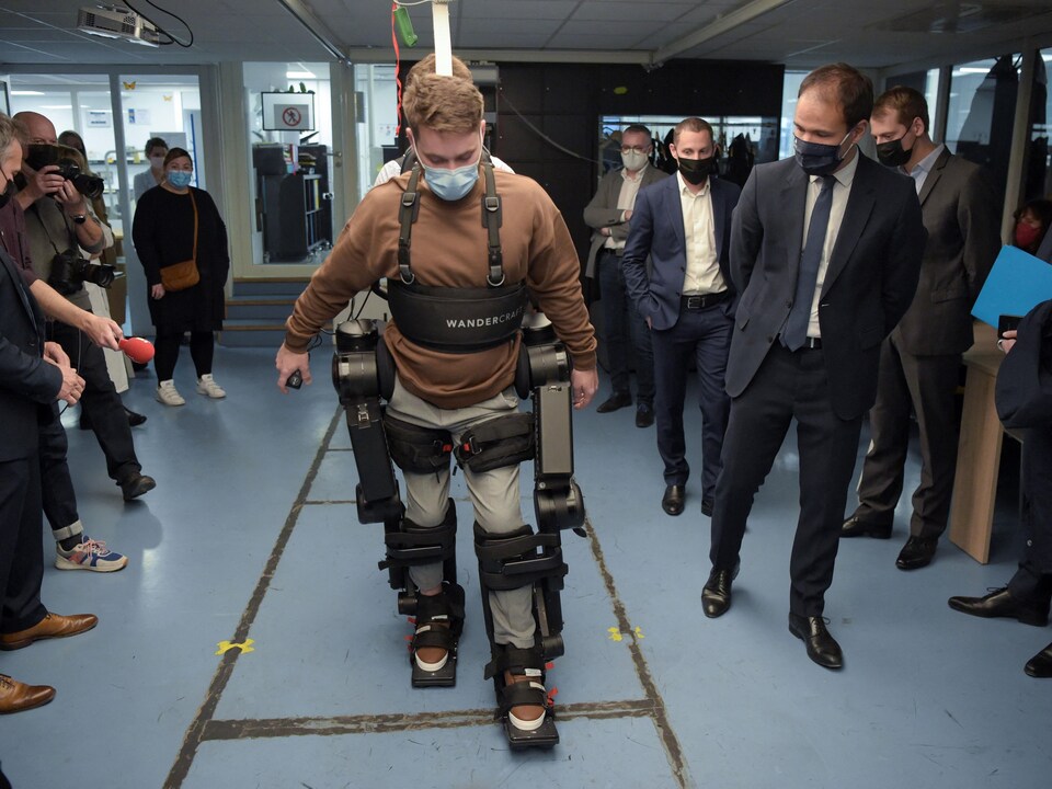 Un homme marche avec un exosquelette, entouré de personnes en complet.