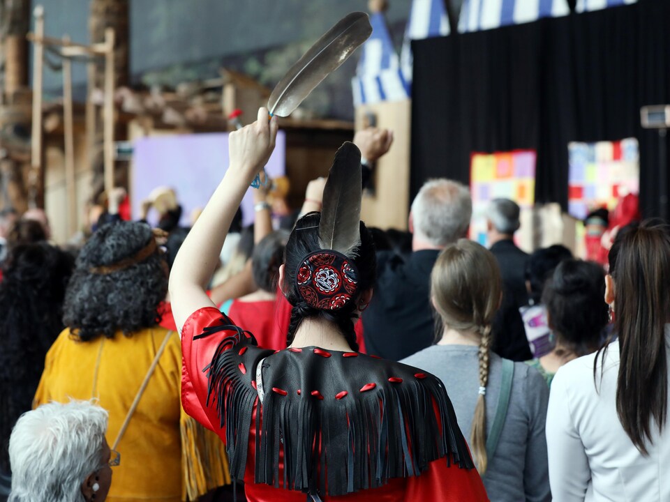 Une femme de dos tient une plume d'aigle pendant la cérémonie de fermeture de l'Enquête nationale sur les femmes et les filles disparues et assassinées.