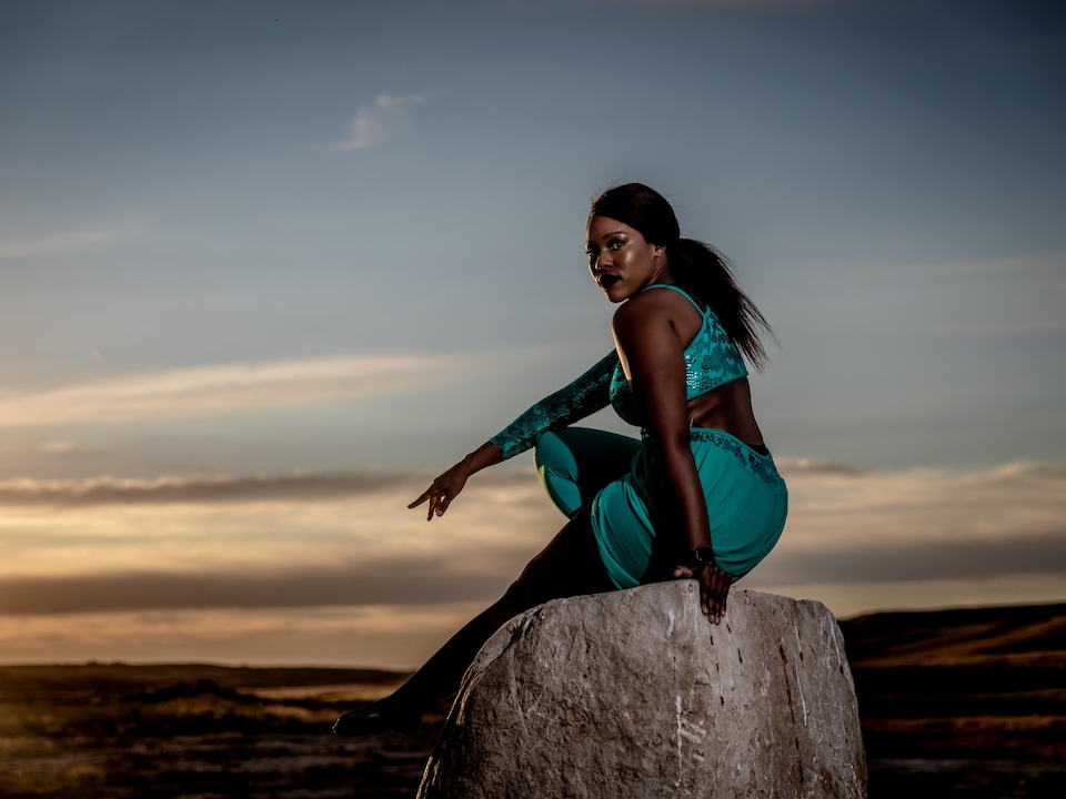 La danseuse Flany Ba de Regina est assise sur une roche au milieu d'une vallée au couché du soleil.