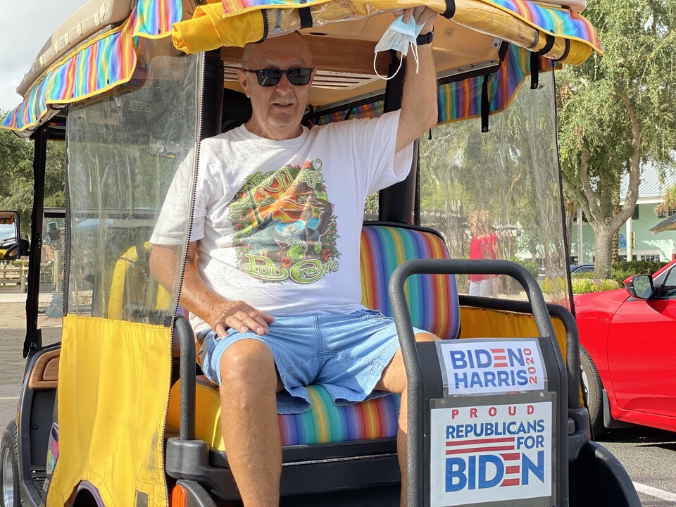 Un homme sur une voiturette de golf arborant une affiche de républicains qui appuient Joe Biden.